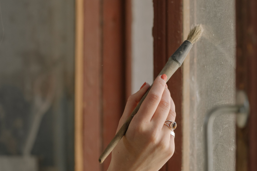 Nahaufnahme einer Frauenhand die ein Holzfenster streicht